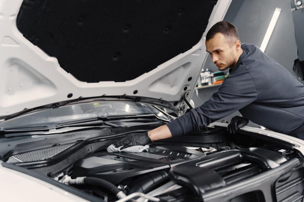 a man cleaning the engine bay of a car. Regular cleaning and maintenance of a car's engine can help ensure it runs efficiently.