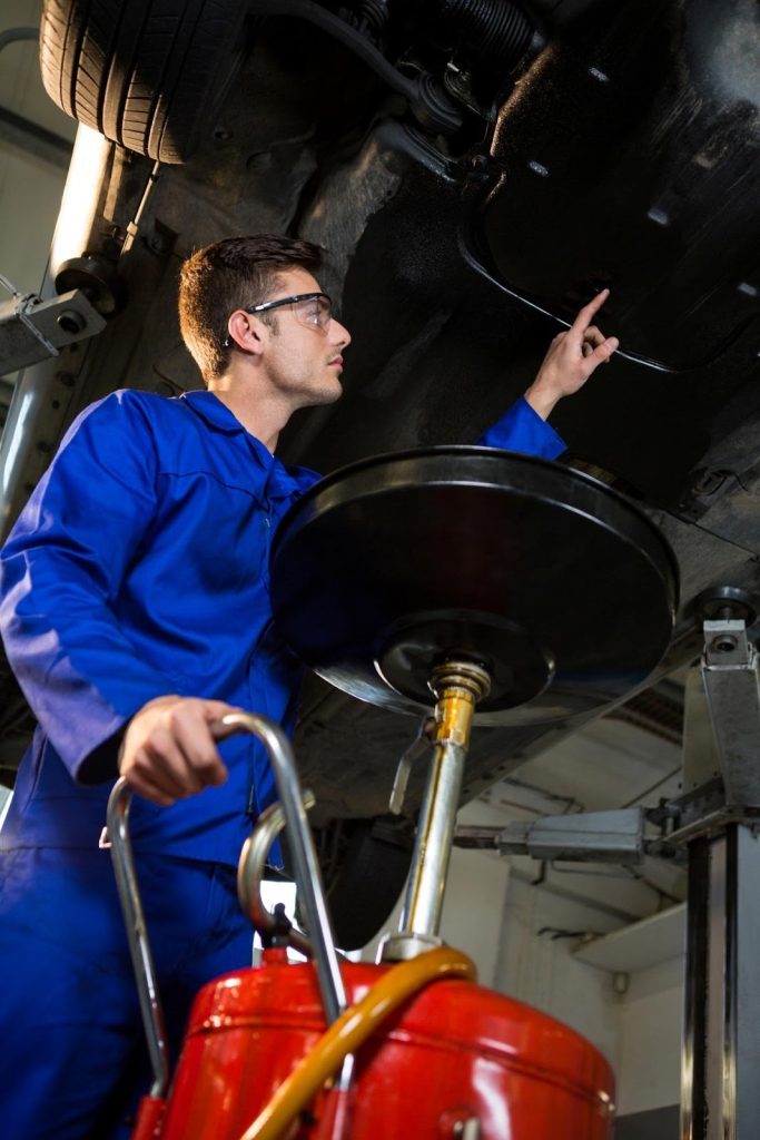an automotive mechanic working on a car that is elevated on a hydraulic lift.