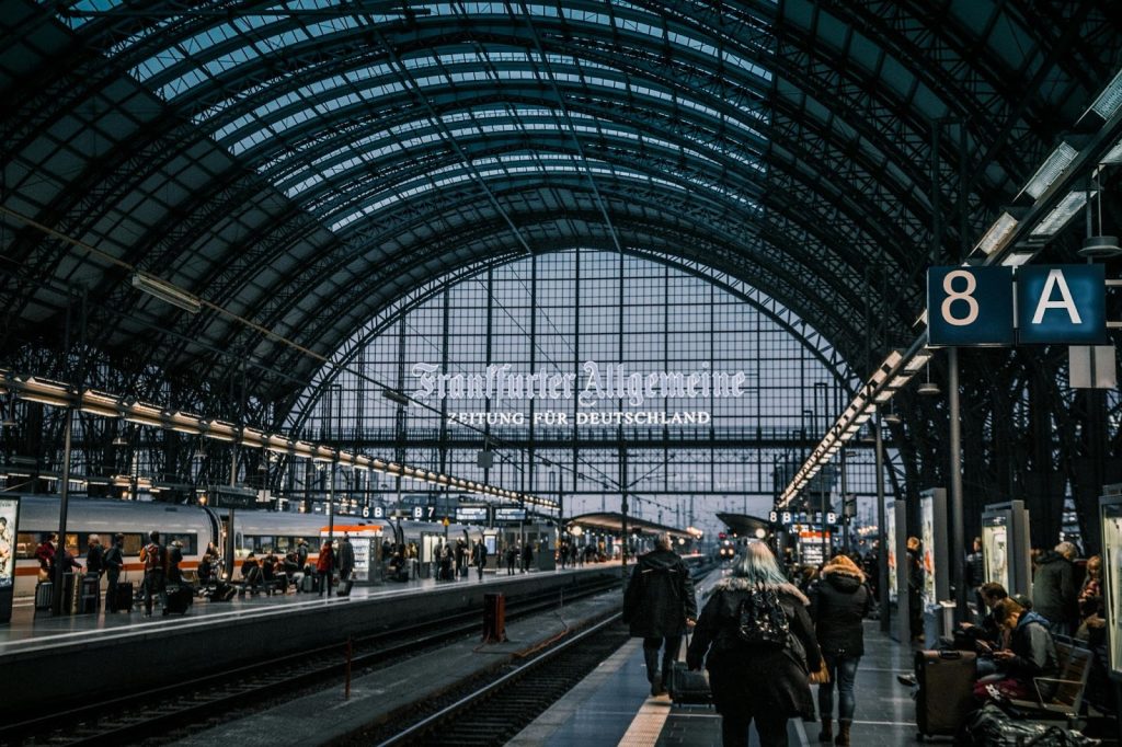 Travelers walking through Frankfurt train station beneath a large arched glass roof.