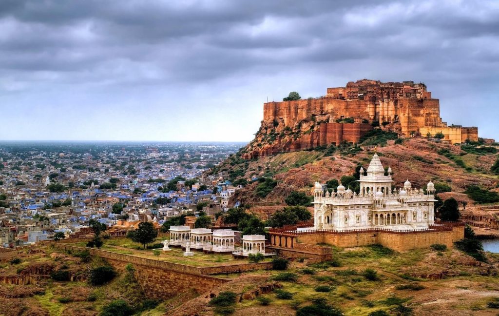 Jaswant Thada and Mehrangarh Fort overlooking the blue city of Jodhpur under a cloudy sky.