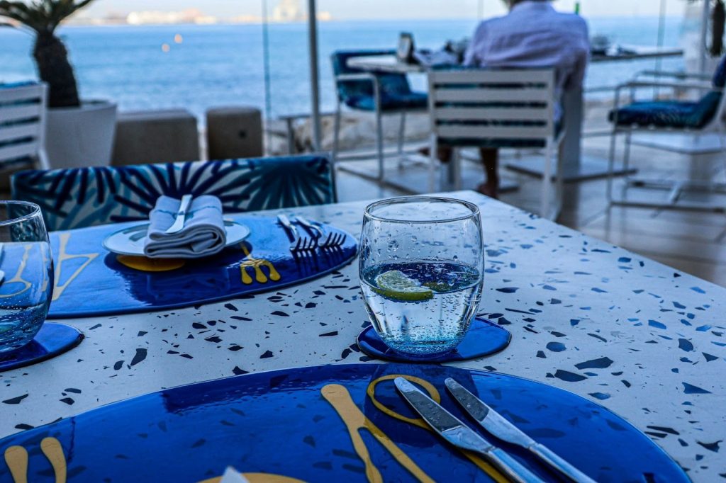 Seaside restaurant table set with vibrant blue and white decor, overlooking the ocean at a luxury resort.