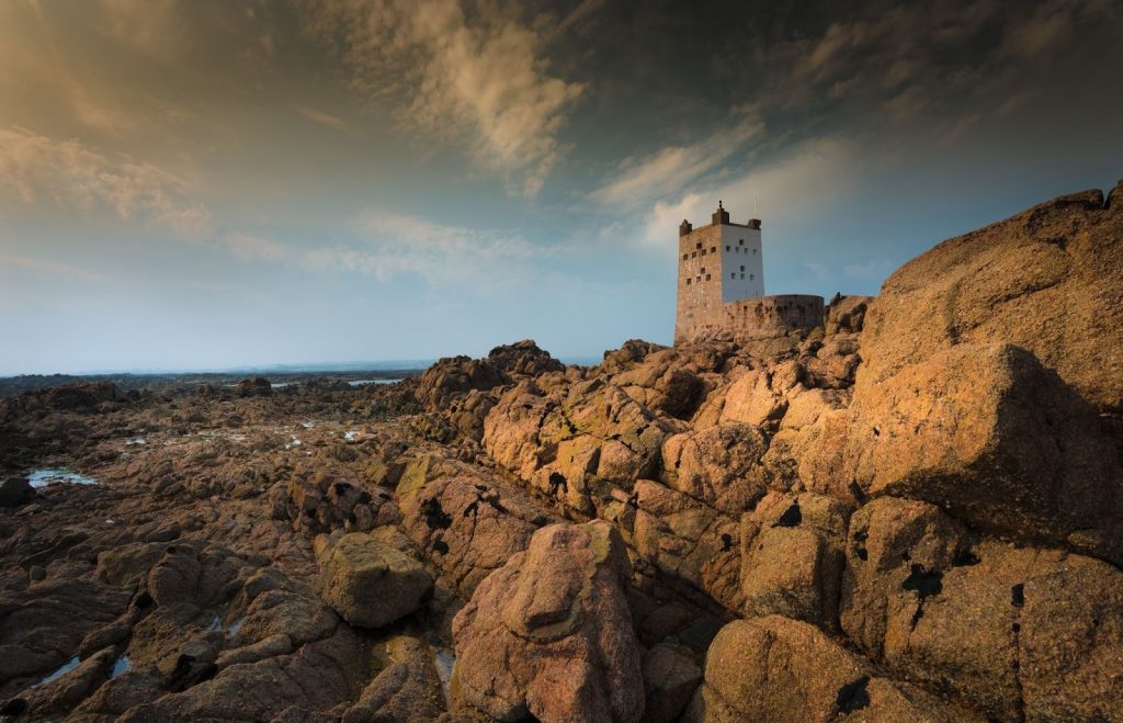 Historic white coastal defense tower perched on rugged brown granite boulders at sunrise or sunset.