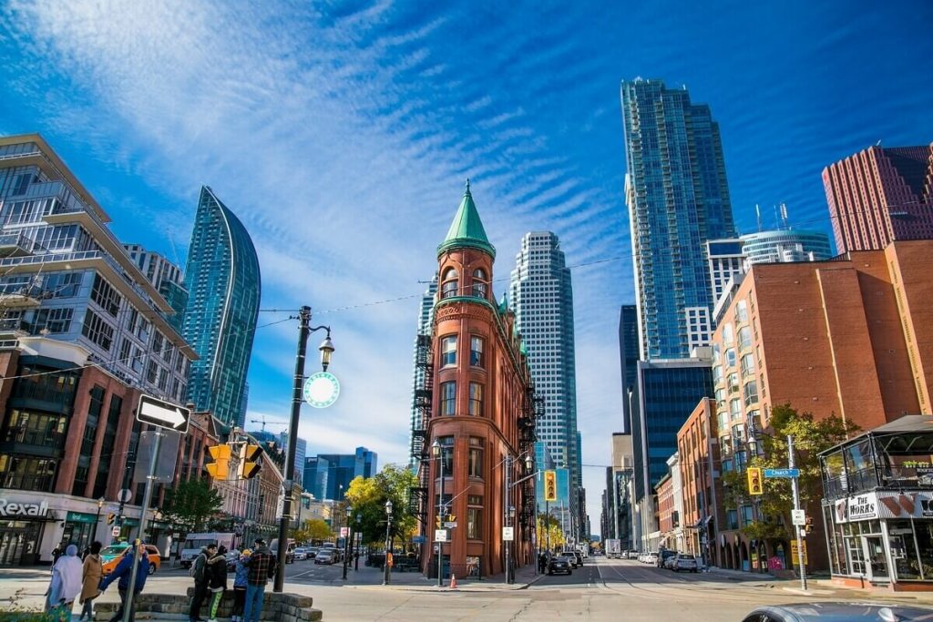 Historic red-brick Gooderham Flatiron Building surrounded by modern glass skyscrapers in downtown Toronto.