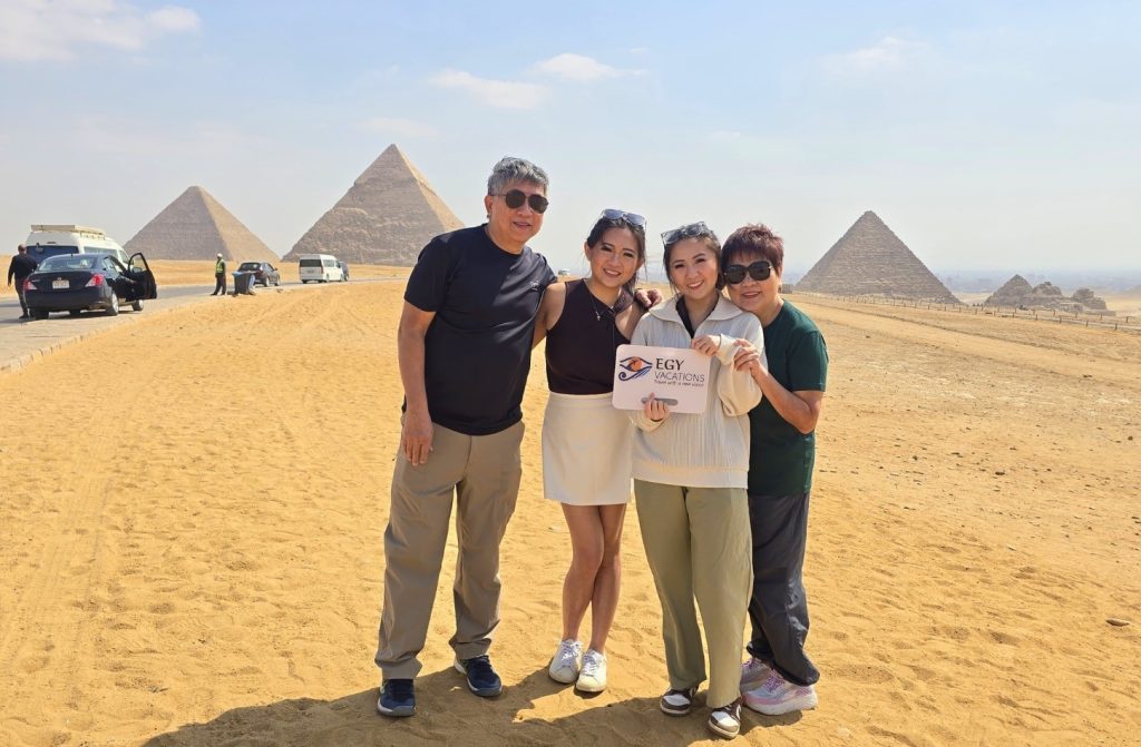 Family of four tourists posing on the sand at the Giza Pyramids in Egypt, holding an EGY VACATIONS sign.