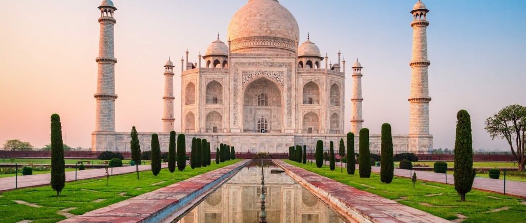 Taj Mahal mausoleum at sunrise, with reflecting pool and cypress trees in Agra, India.