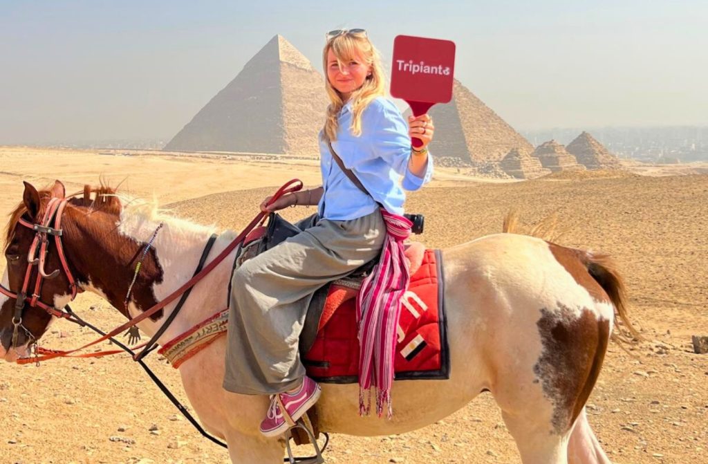 Woman on horseback holding a "Tripants" sign with the ancient Pyramids of Giza in the desert background.