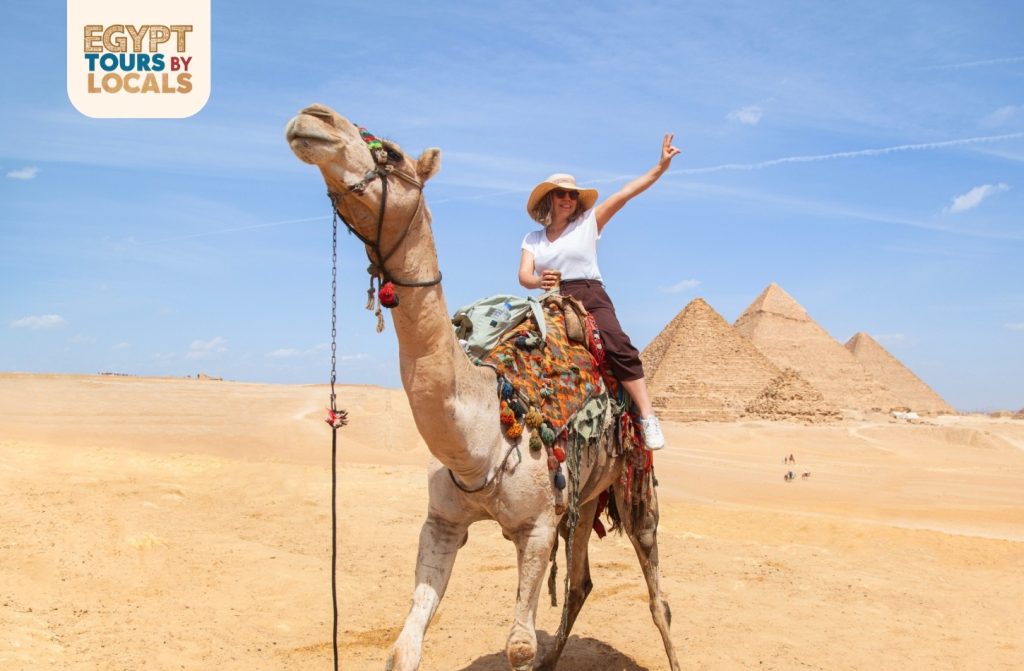 Woman riding a camel in front of the Pyramids of Giza in Egypt under a clear blue sky.