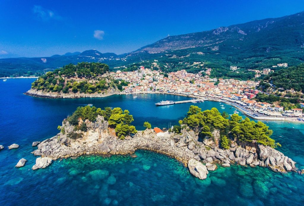 Aerial view of Parga, Greece, featuring the Islet of Panagia, turquoise waters, and a colorful harbor town.