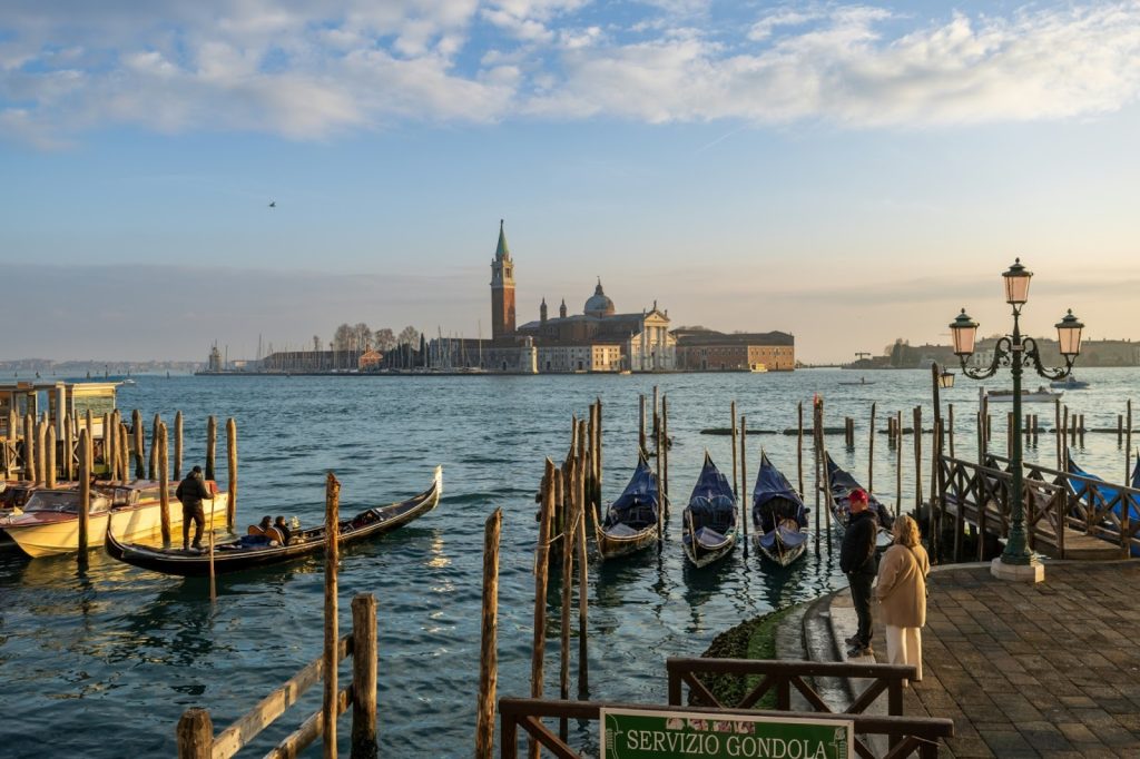 Moored gondolas and San Giorgio Maggiore island at sunset in Venice, Italy, with a gondolier in the lagoon.
