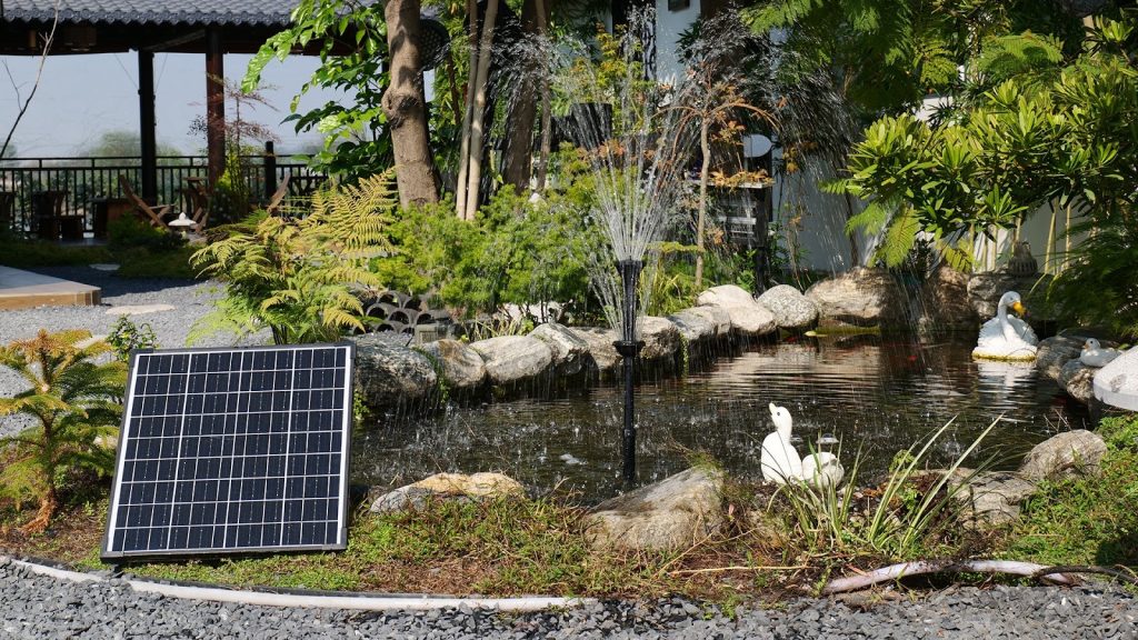 Solar powered pond fountain with a multi-tier spray head and solar panel in a stone-lined garden pond.