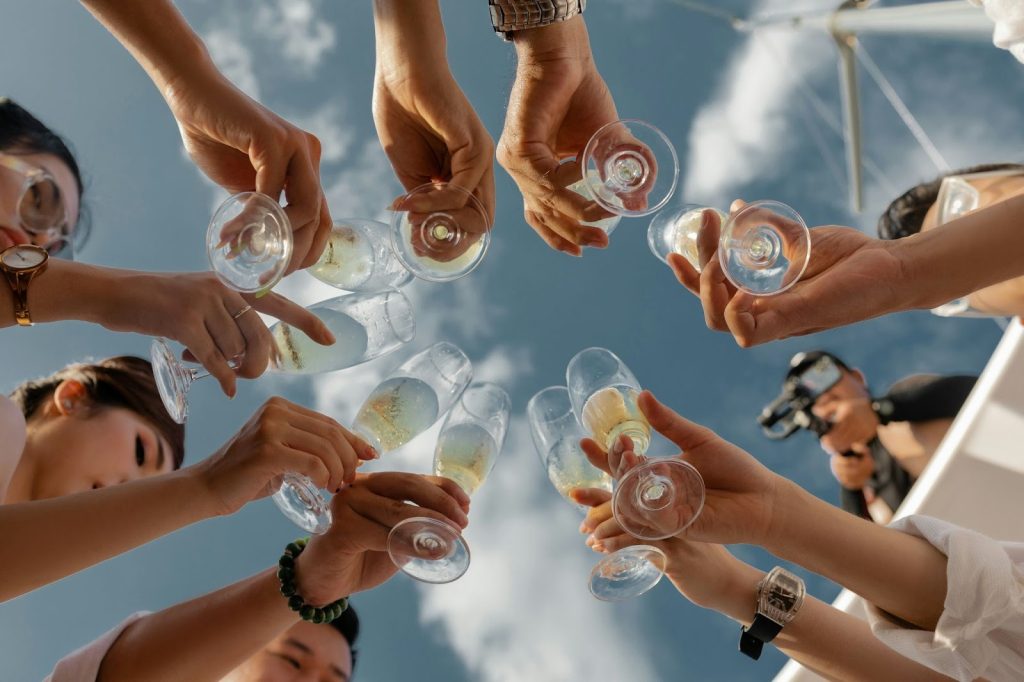 Low-angle view of a group of people toasting with champagne flutes against a blue sky on a sunny boat deck.