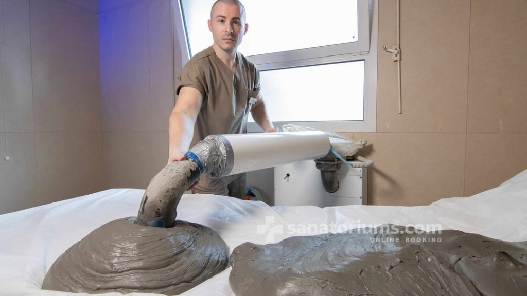 A therapist applying thick medicinal mud to a treatment table using a specialized applicator pipe.