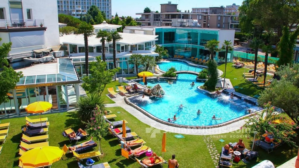 Aerial view of a luxury resort pool with turquoise water, sun loungers, and palm trees under a bright sun.