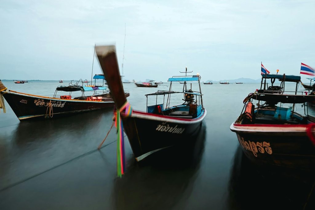 Traditional Thai long-tail boats with colorful ribbons anchored in calm twilight waters under a blue sky.