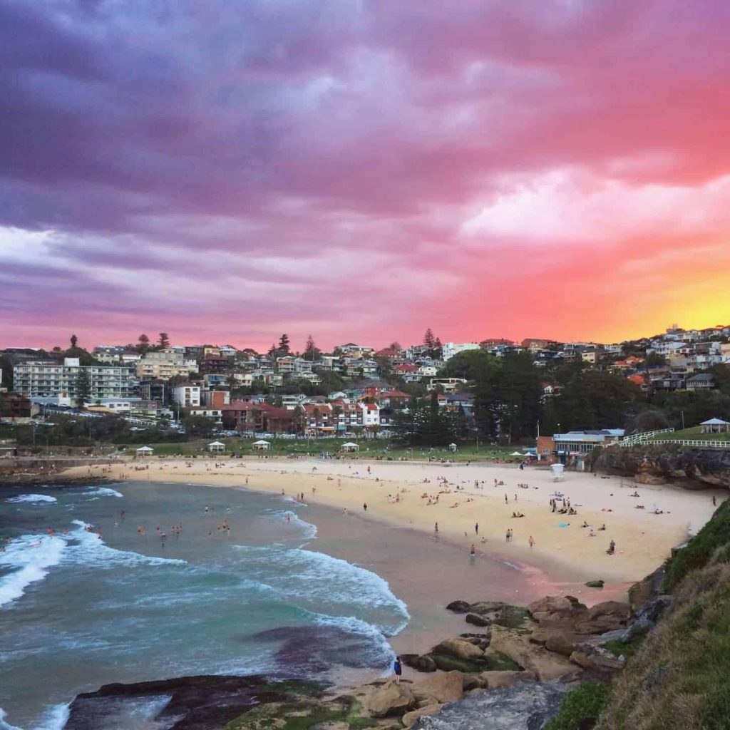 Sydney Vibrant purple and orange sunset over a crowded sandy beach and hillside town with rolling ocean waves in Sydney