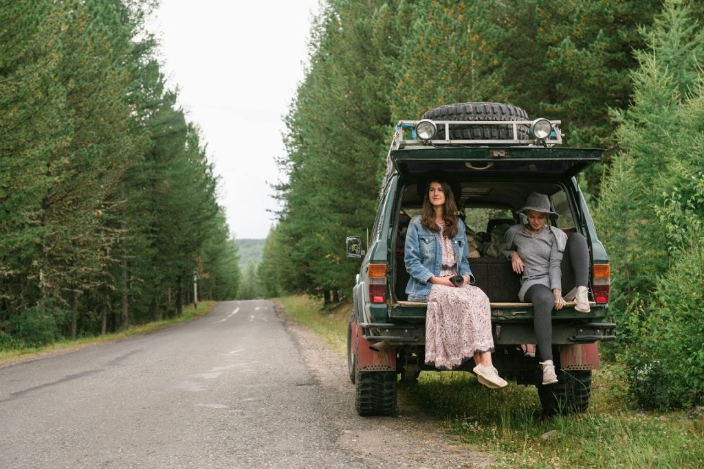 Two women sitting in the back of an off-road SUV on a forest road during a scenic road trip.