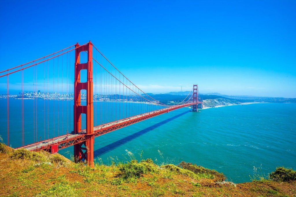 Wide-angle view of the Golden Gate Bridge stretching across turquoise water toward the San Francisco skyline.