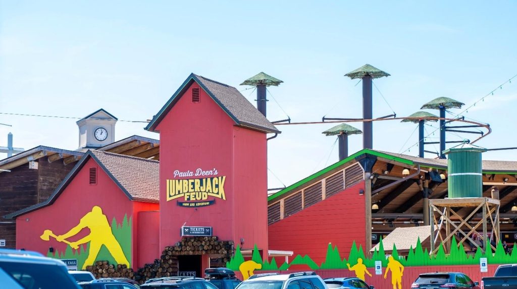 Exterior of Paula Deen's Lumberjack Feud in Pigeon Forge featuring red barn buildings and adventure park towers.