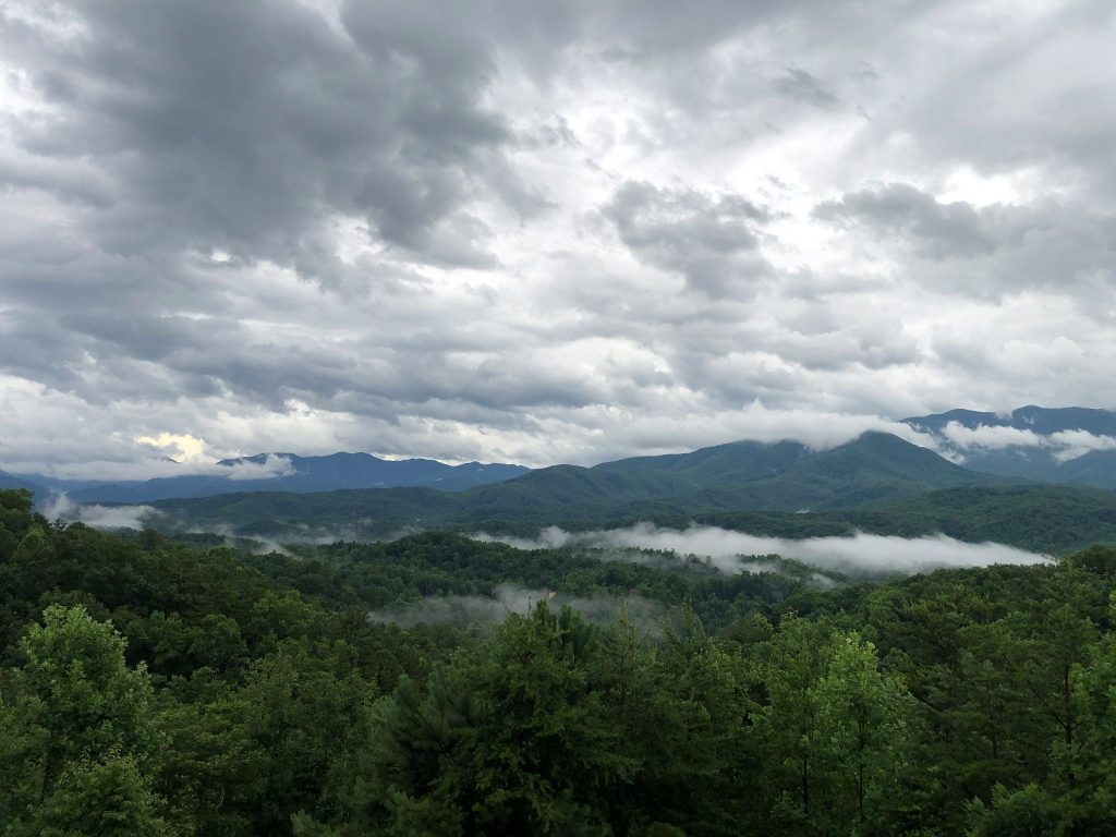 Lush green mountain ridges layered behind low-hanging valley mist under a dramatic, cloudy grey sky in the Great Smoky Mountains