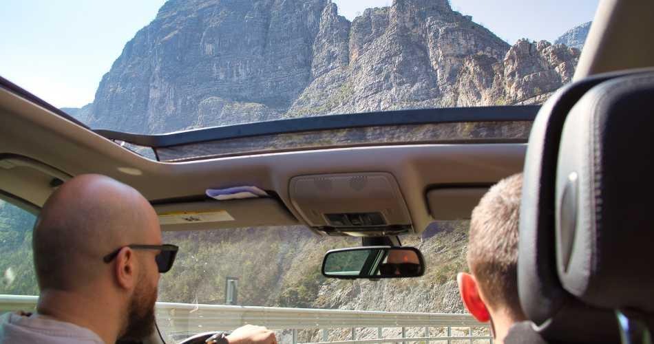 View through a car's open sunroof of a massive, craggy mountain during a scenic road trip.