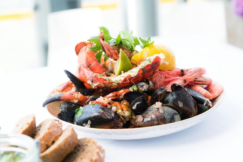 Gourmet seafood platter featuring steamed mussels, whole shrimp, and lobster with lemon and lime on a white table.