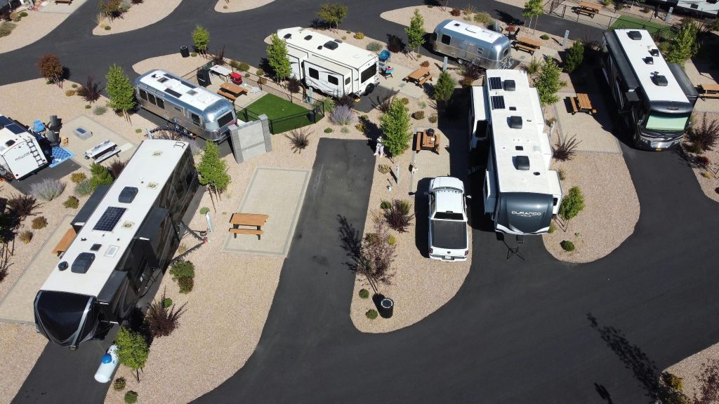 Aerial drone view of a luxury RV resort featuring diverse motorhomes and travel trailers parked in paved campsites.