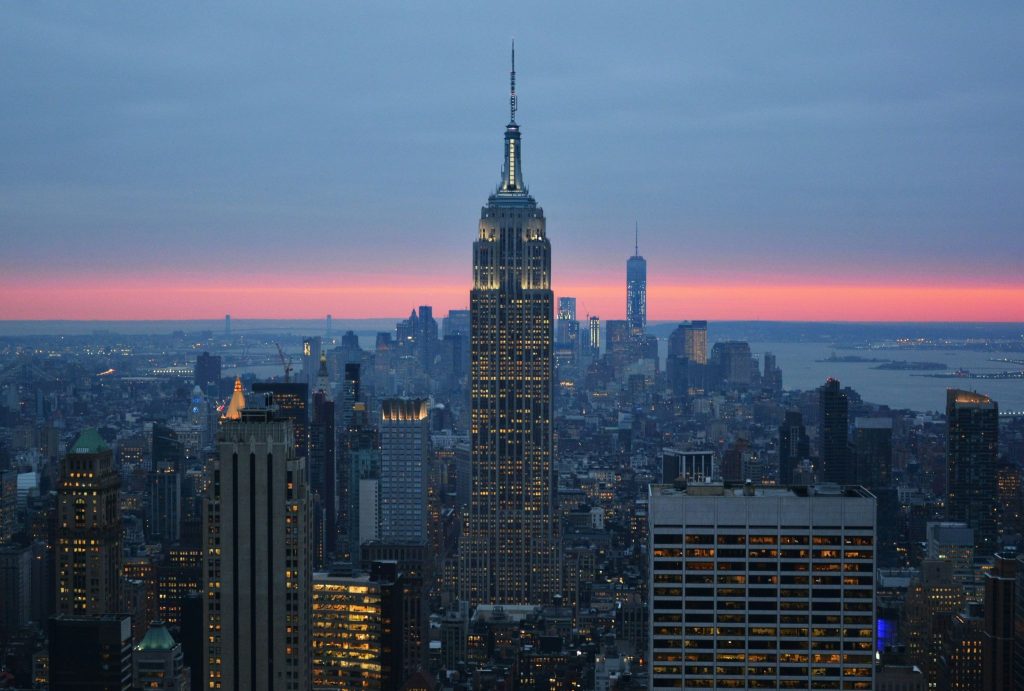 Illuminated Empire State Building towering over the New York City skyline at dusk, set against a vibrant pink sunset.