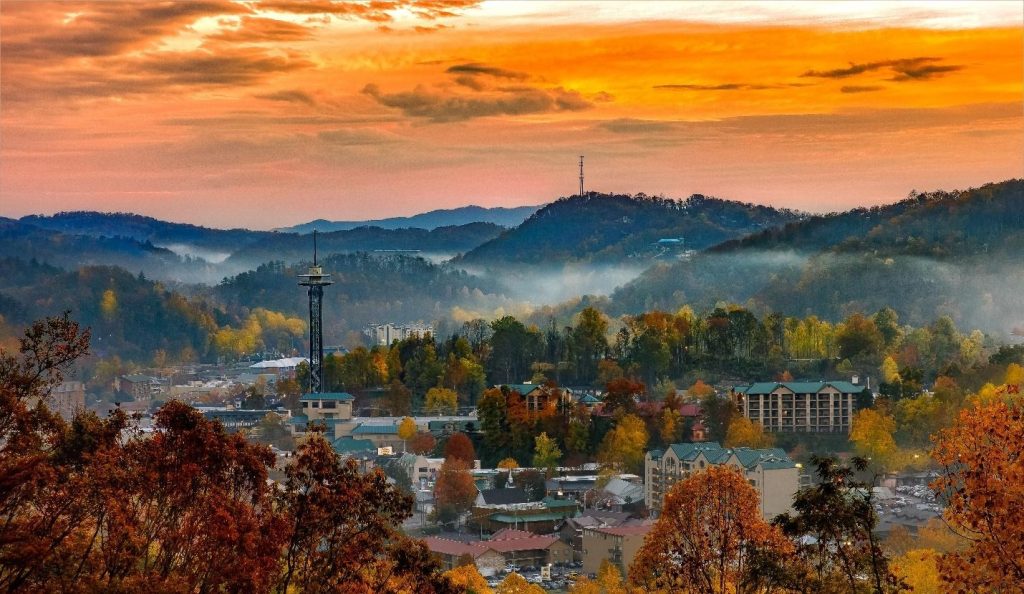 Autumn view of Gatlinburg in the Smoky Mountains, featuring the Space Needle, vibrant fall foliage, mist, and a fiery sunset.