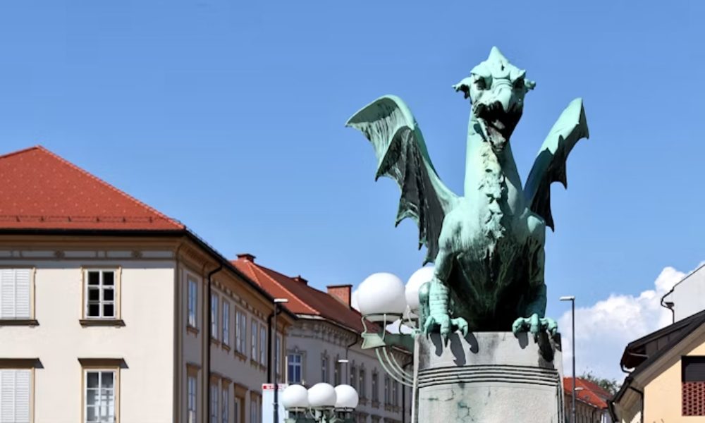 Oxidized green copper dragon statue with spread wings on the Dragon Bridge in Ljubljana, Slovenia, against a clear blue sky.