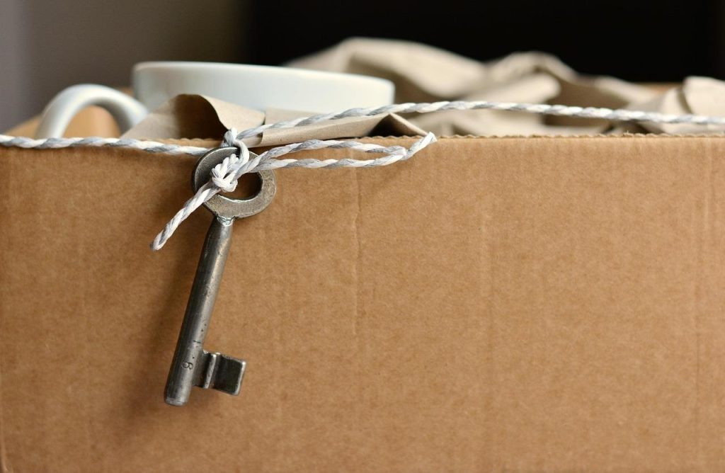 Close-up of a brown cardboard moving box tied with twine, featuring a vintage metal skeleton key hanging from the side.