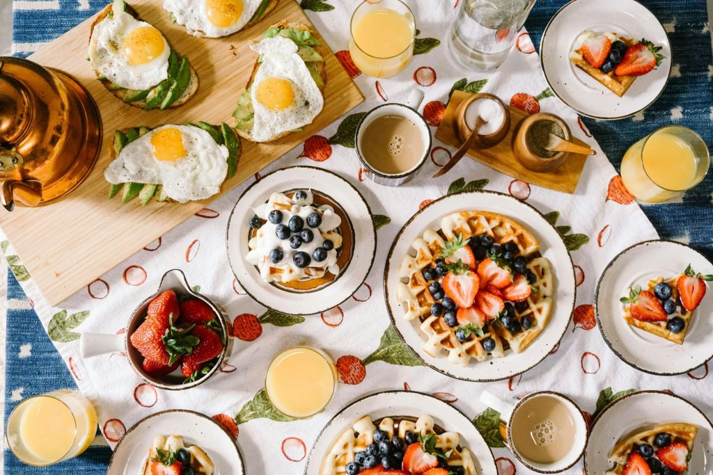 Flat-lay of a lavish brunch spread featuring avocado toast with fried eggs, berry Belgian waffles, orange juice, and coffee.