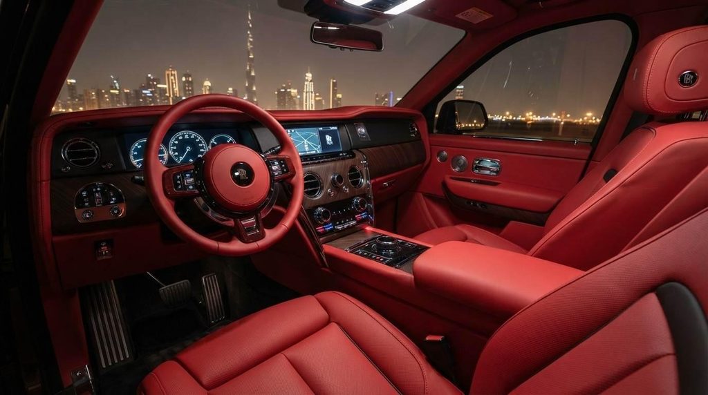 Red leather Rolls-Royce interior at night, viewing the illuminated Dubai skyline and Burj Khalifa through the windshield.