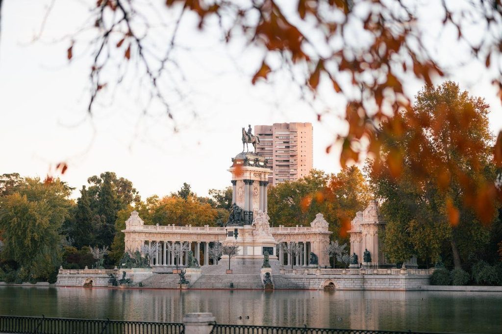 Monument to Alfonso XII overlooking the Estanque Grande (Great Pond), framed by blurred orange autumn leaves under warm golden light in inside El Retiro Park in Madrid, Spain