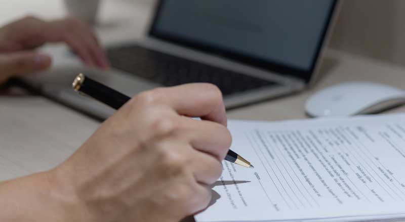 a hand holding black pen writing on application at home office
