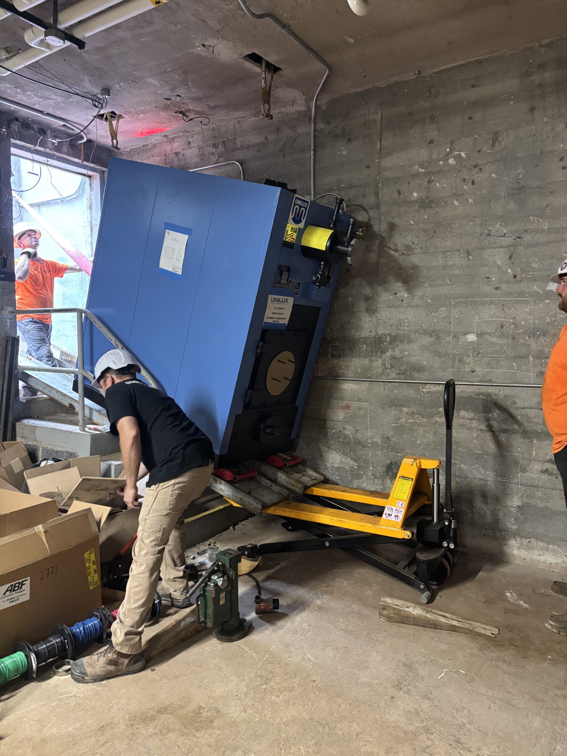 Trimble Services crew guiding a boiler into the basement during the Starbuck Elementary boiler rigging project.