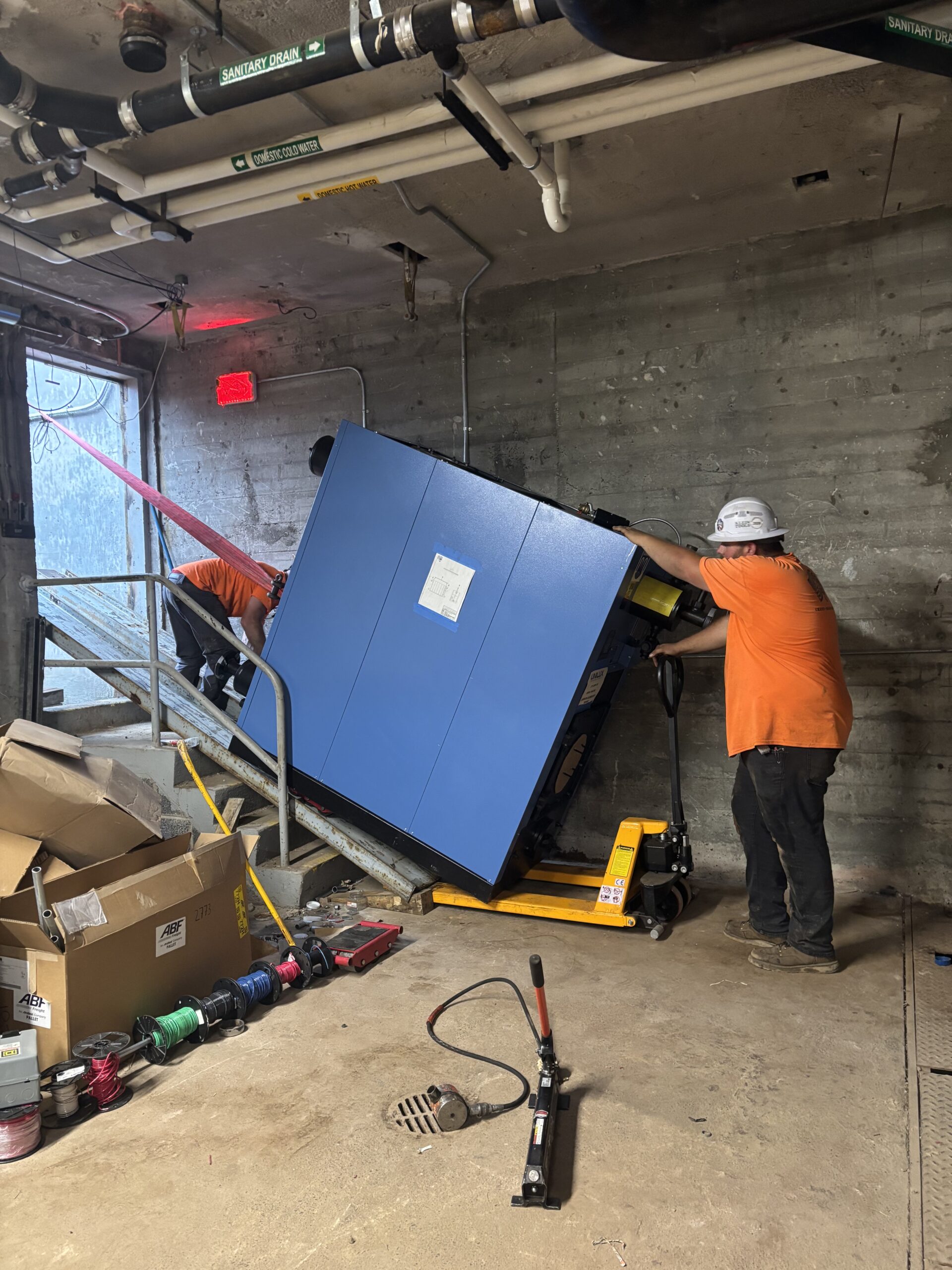 Trimble Services crew guiding a boiler into the basement during the Starbuck Elementary boiler rigging project.