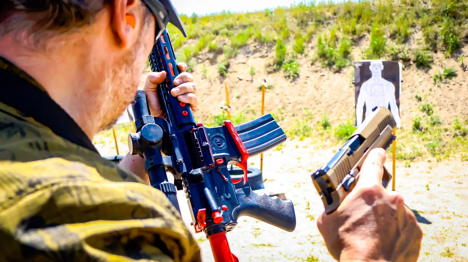 Man performing a rifle-to-handgun transition drill at an outdoor shooting range with a human silhouette target in the background.