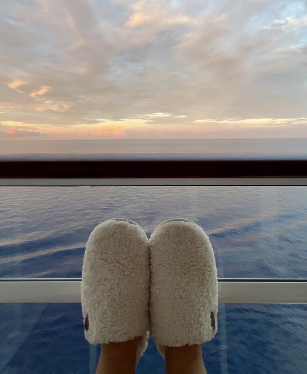 Cozy slippers propped on a cruise ship balcony railing at sunset over the open sea