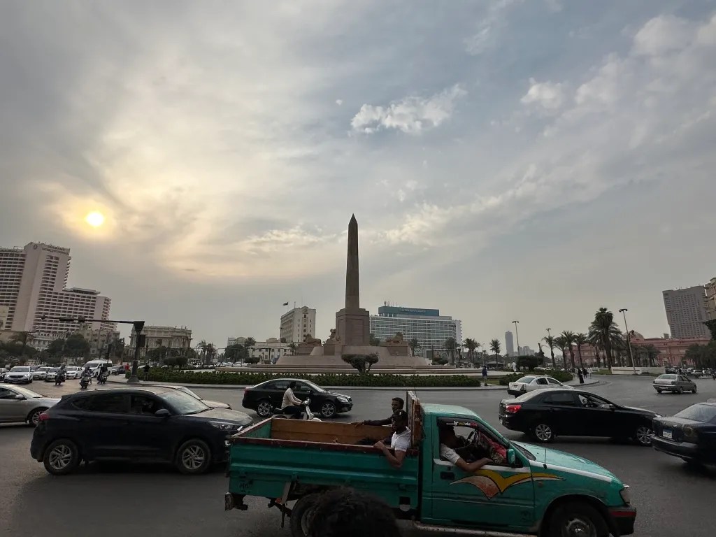 Traffic and an obelisk in Cairo beneath a hazy afternoon sky