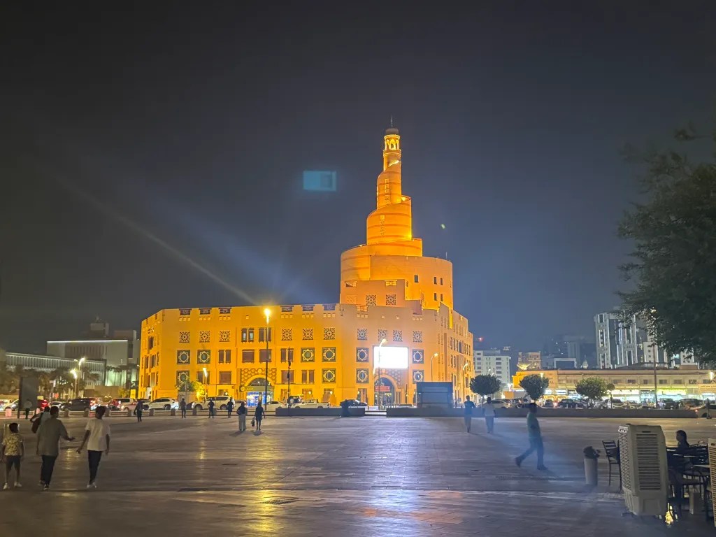 An illuminated spiral tower and surrounding buildings near Souq Waqif in Doha at night