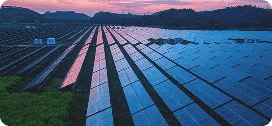 Rows of solar panels in a solar farm at sunset with a pink-orange sky in the background.