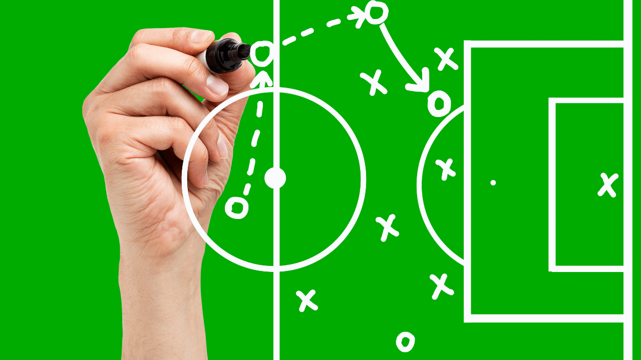 Coach's hand drawing a soccer tactics play on a green field diagram with X and O markings and a circular center circle