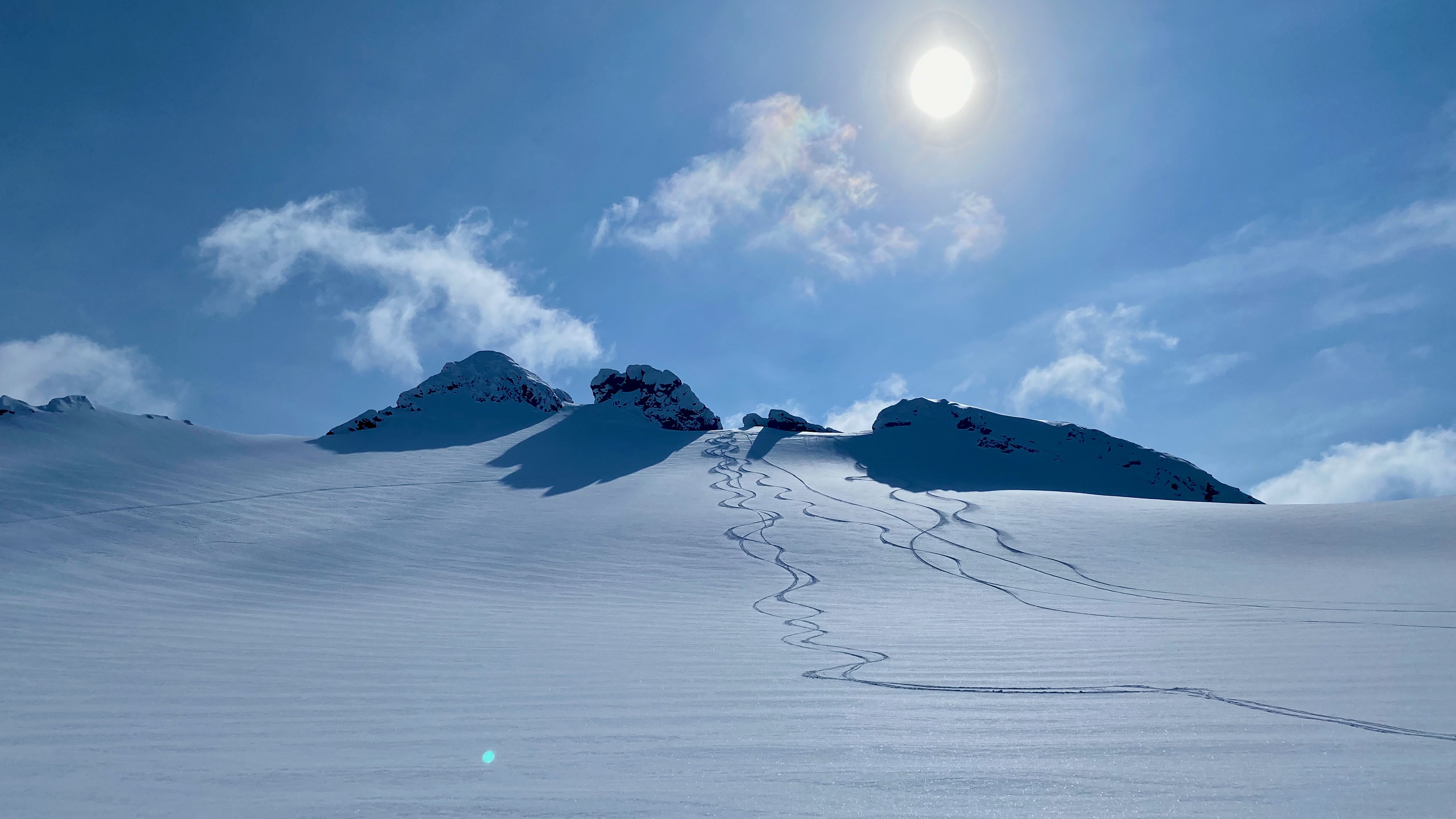 Ski tracks down an open snow slope under the sun
