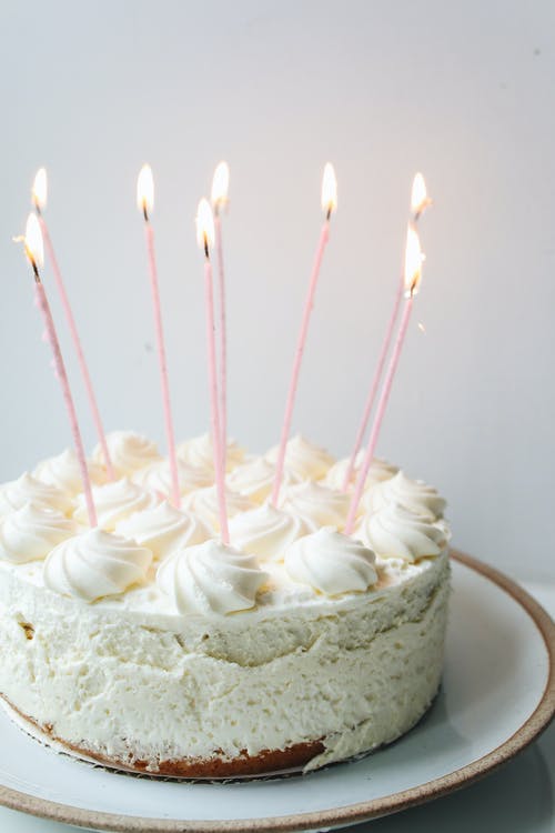 CREAMY, LUCIOUS BIRTHDAY CAKE WITH WHITE ICING AND SEVERL LONG LIT CANDLES