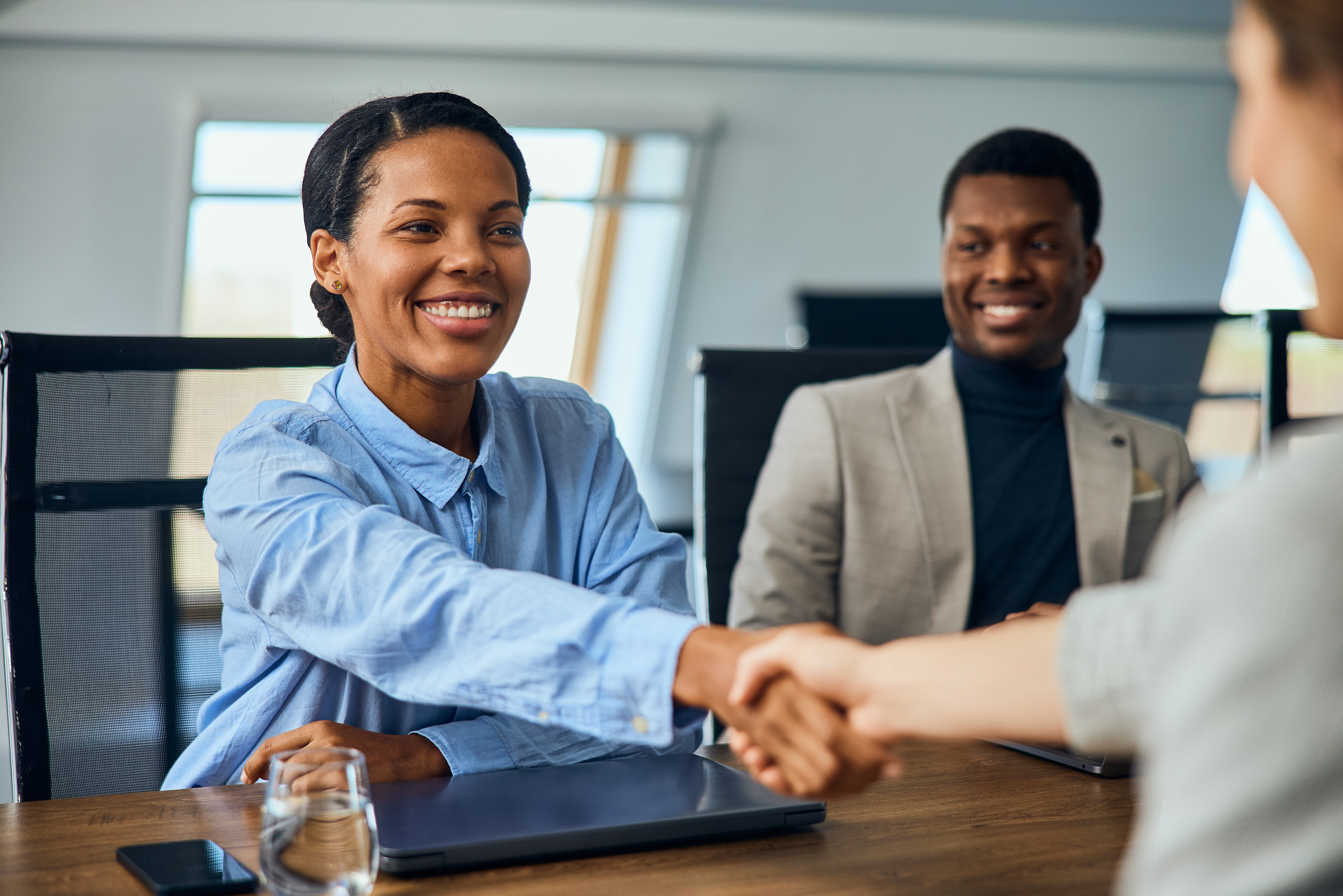 A happy black businesswoman made a deal with another client, doing a handshake.