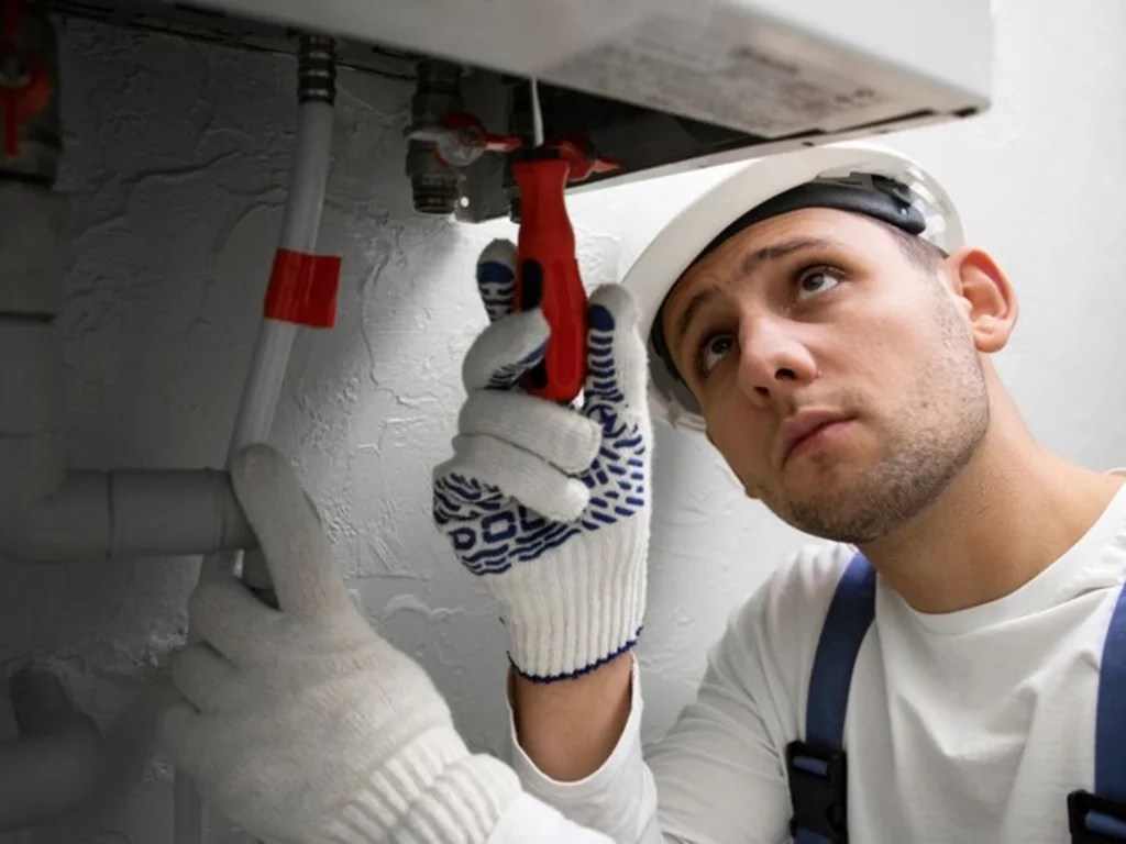 Emergency plumbing services technician tightening a leaking valve with a wrench