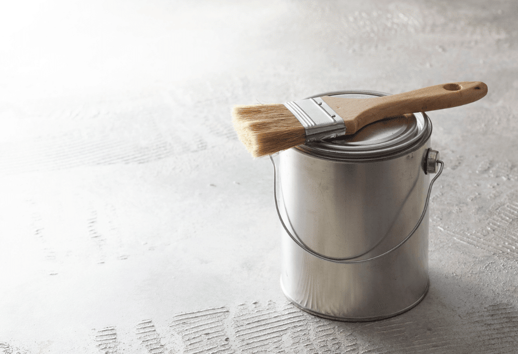 Paint can and paintbrush on a floor, representing practical DIY ideas for storing and reusing leftover paint after a painting project.