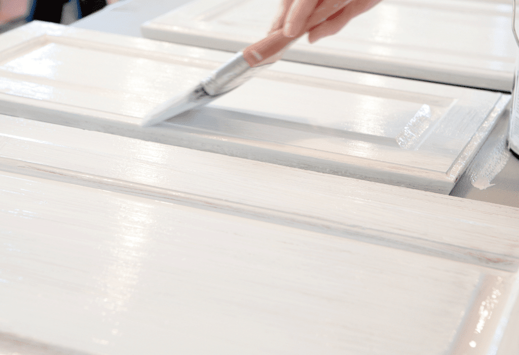 Applying white paint to cabinet doors with a brush during a cabinet painting project.
