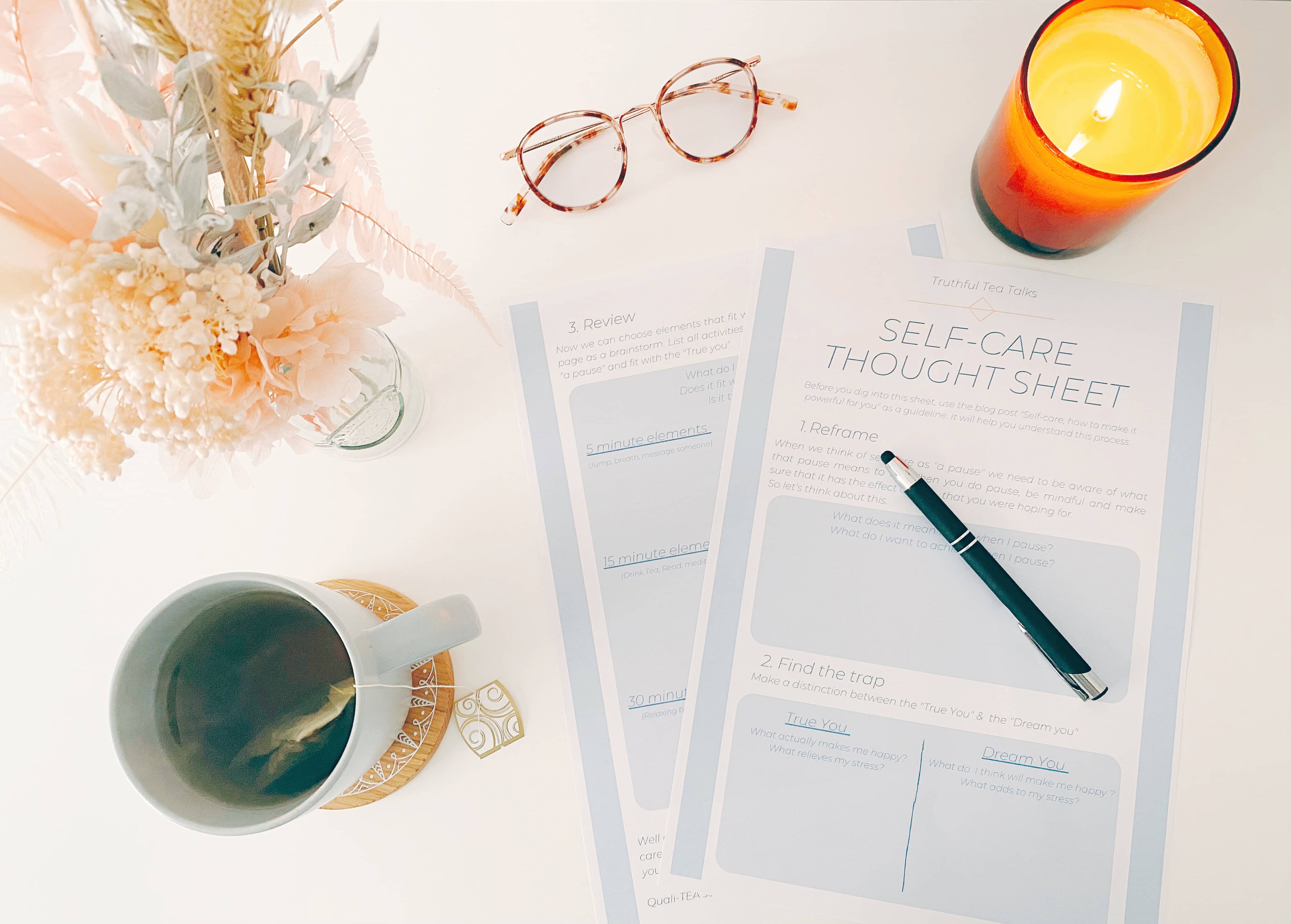Flat lay of a self-care thought sheet with a pen, tea, candle, and pastel flowers – a calming setup for redefining self-care for mums.