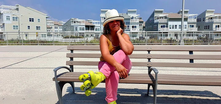 La Frae Sci sitting on a bench outdoors, in roller skates